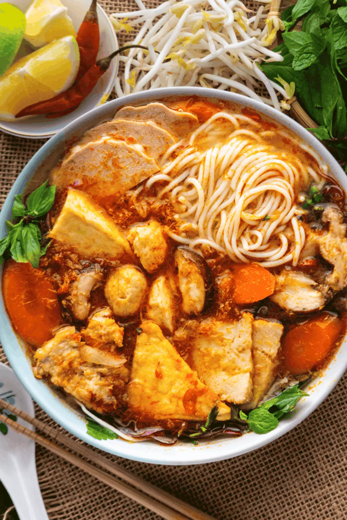 Noodles, mushrooms and tofu in a bowl of soup with carrots and mint